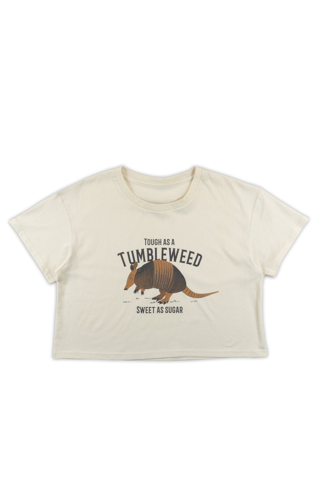 Beige t-shirt with armadillo graphic and text that says "Tough as a tumbleweed, Sweet as sugar" on a white background.