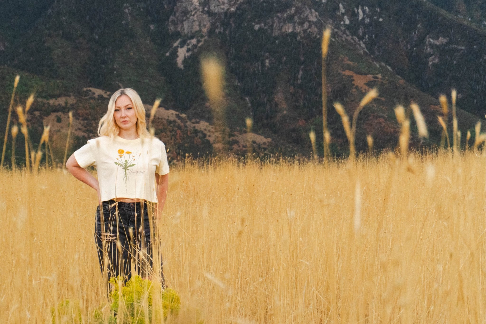 Person standing in a field of tall grass with mountains in the background