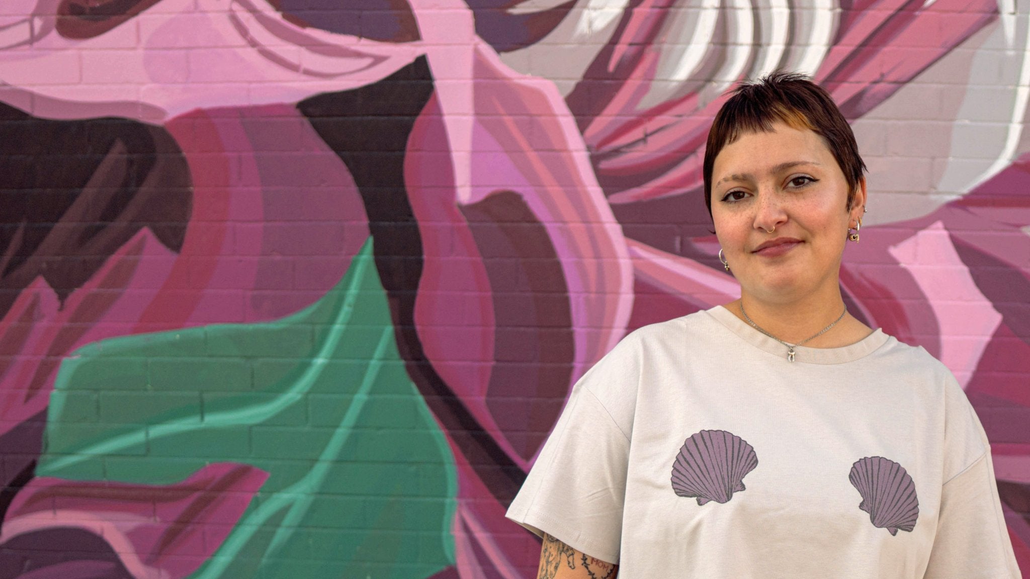 Person wearing a white shirt with shell designs in front of a colorful mural.