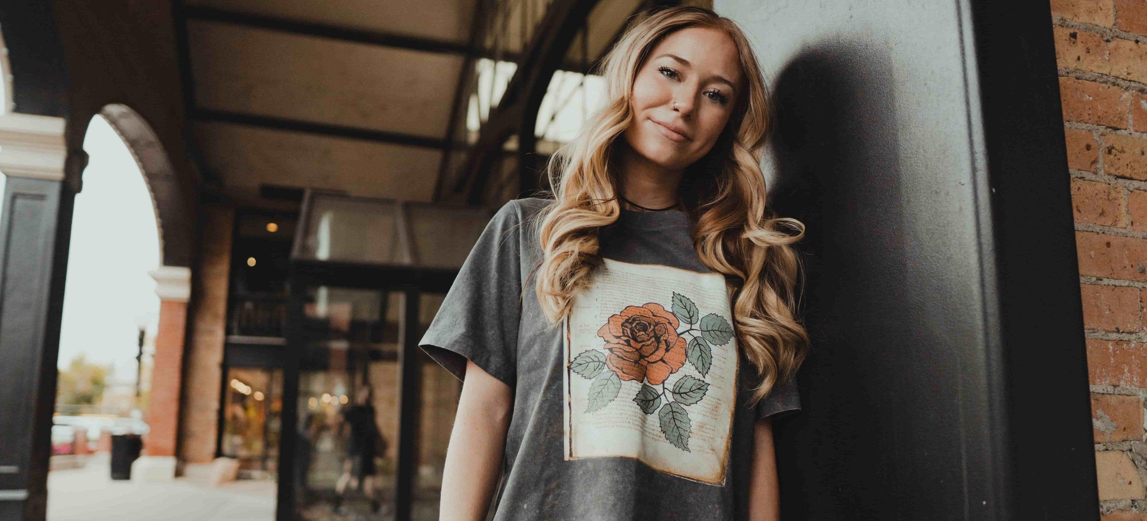 Woman wearing a gray t-shirt with a floral design, standing outdoors.
