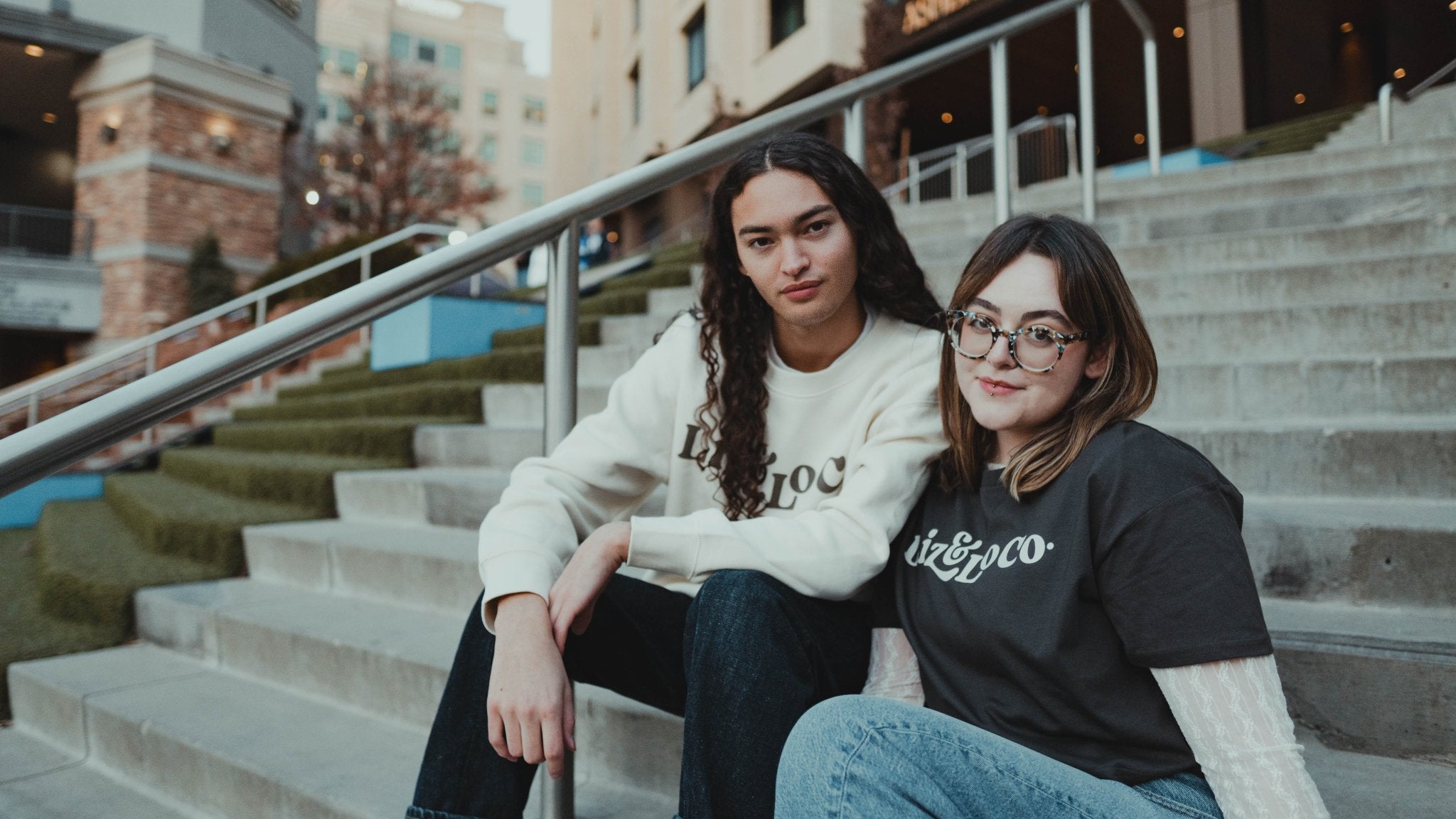 Two people sitting on steps in an urban setting with a building in the background.