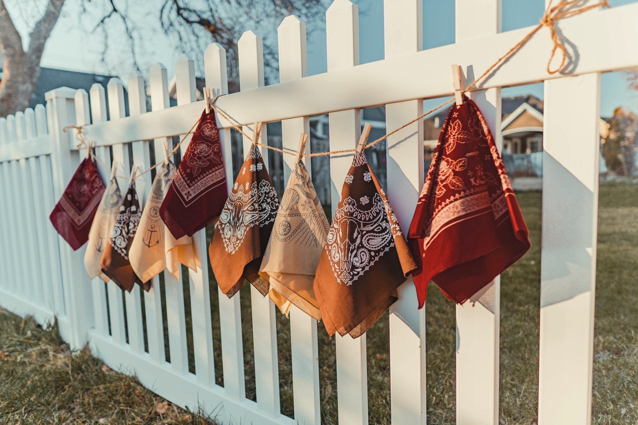 Colorful bandanas hanging on a clothesline against a white picket fence.