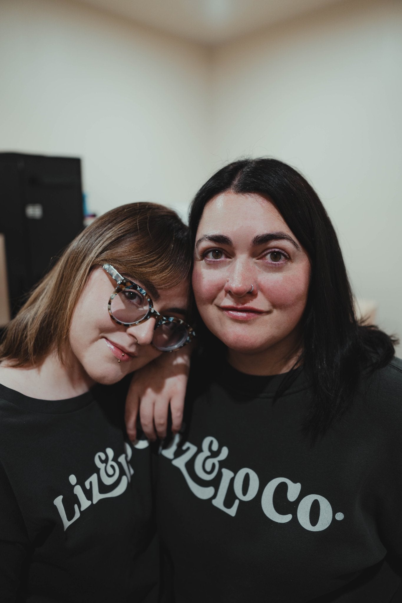 Two people wearing black sweatshirts with 'Liz & Co' text, posing closely together.